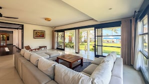 A spacious living room with a large sofa, a coffee table, and a view of a pool and garden. - Bougain Villa - 5 Bedroom, Oceanfront villa inc. Chef (Negari, Banjarankan,)
