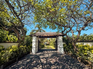 A pathway leading to a covered structure with a tiled roof, surrounded by lush greenery and trees.