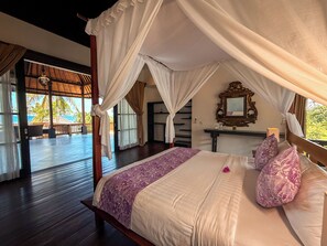 A bedroom with a canopy bed, a wooden floor, a view of the outdoors, and a mirror on the wall.
