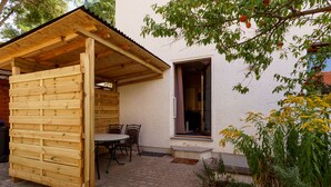 A wooden outdoor seating area with a table and chairs, a covered wooden structure, and a white building with a window. - Vacation home in Arnstadt for up to 8 people more on request (Arnstadt)