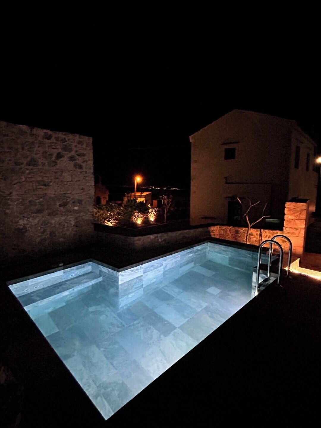 A swimming pool with a glass bottom, surrounded by stone walls and a small building with a light source.