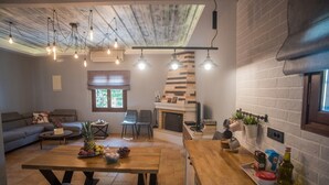 Una sala de estar moderna con sofá, mesa de comedor y sillas. Cuenta con una chimenea, una zona de cocina con lavabo y una ventana con persianas.