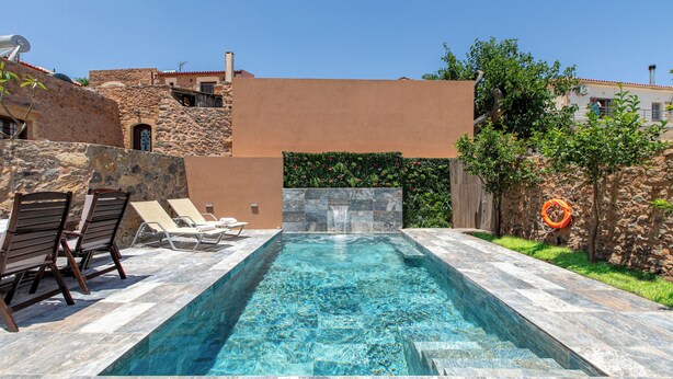 Una piscina rectangular con agua azul cristalina, rodeada de muros de piedra y un techo plano.