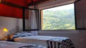 Una camera da letto con due letti, una finestra vista su dolci colline, una lampada e un muro rosso.