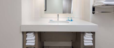 Un baño con lavamanos blanco, espejo y toallero.
