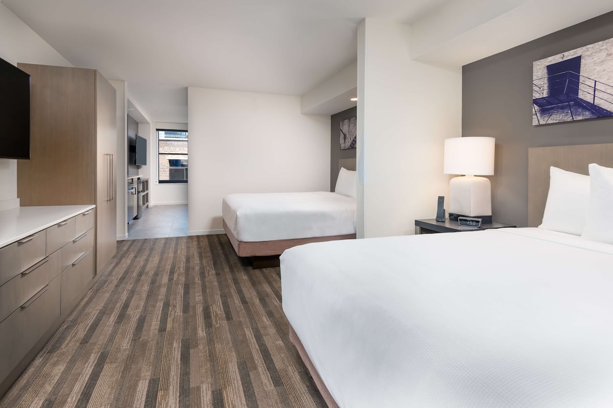 Une chambre d’hôtel avec un grand lit, un lit plus petit, un bureau avec une lampe et un téléviseur fixé au mur.