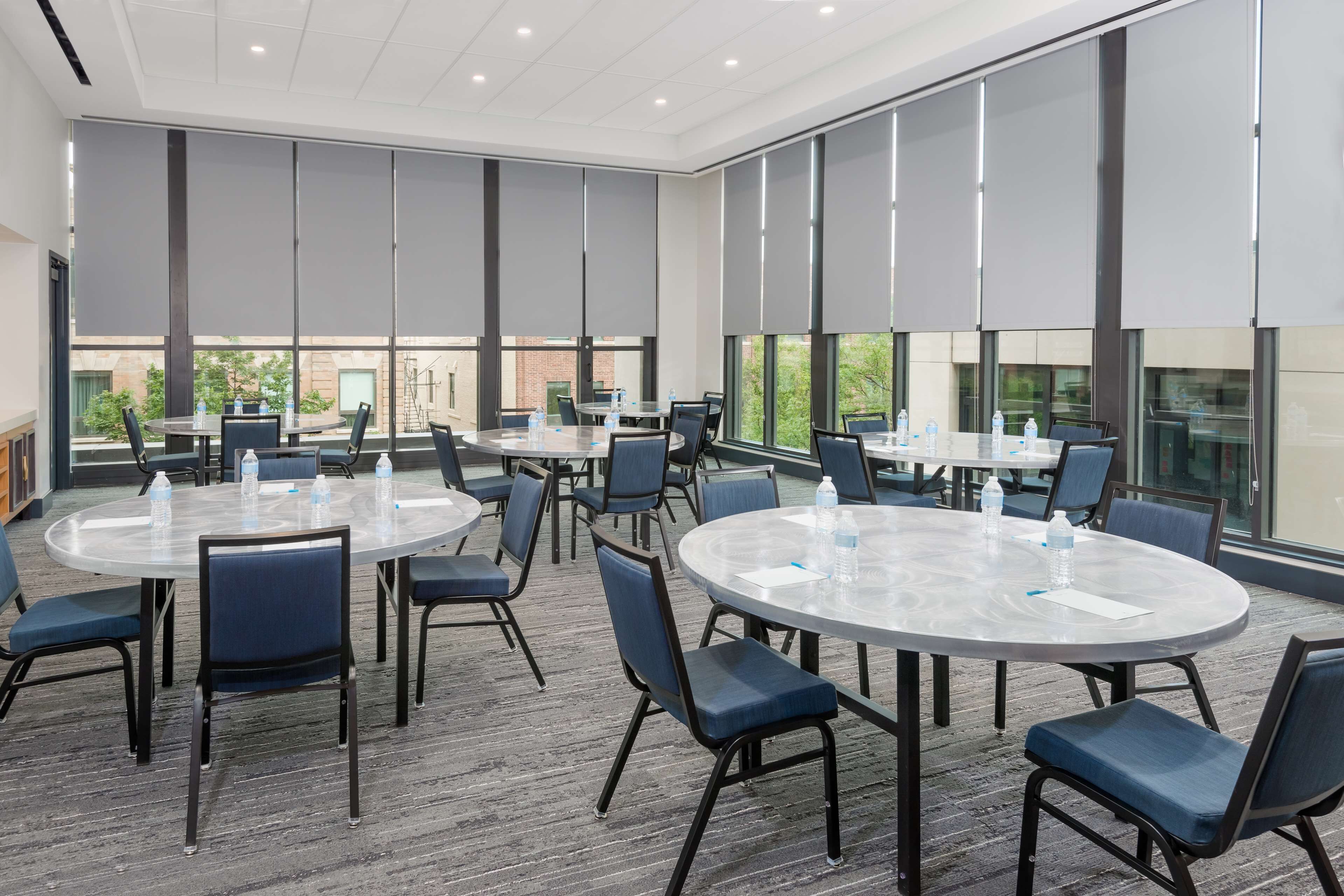 Sala de conferências com mesas redondas, cadeiras e garrafas de água.