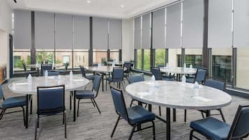 Sala de conferências com mesas redondas, cadeiras e garrafas de água.