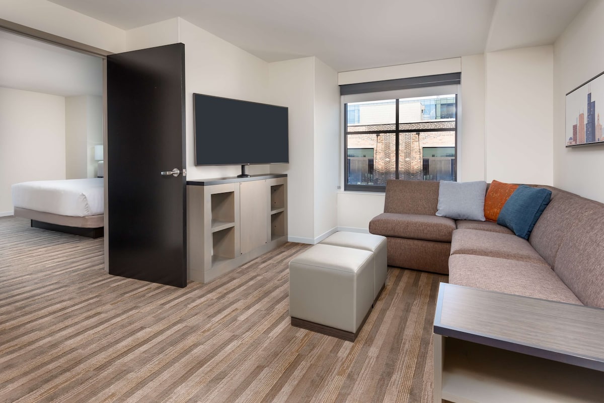 Une chambre d’hôtel moderne dotée d’un grand lit, d’un canapé, d’une télévision et d’une fenêtre donnant sur la ville.