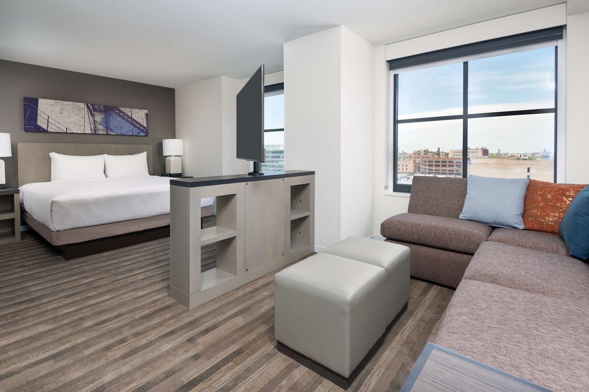 Une chambre d’hôtel équipée d’un lit, d’un bureau, d’un canapé et d’une grande fenêtre donnant sur la ville.