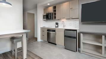 Una cocina moderna con microondas, horno y refrigerador integrados, una encimera blanca y una mesa de comedor de madera con banco.