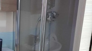 A shower with a glass door, a white sink, and a wooden cabinet.