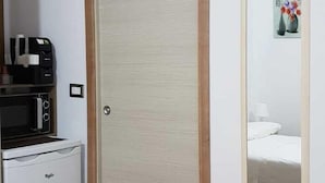 A compact room with a wooden door, a small kitchenette with a microwave and refrigerator, and a wall-mounted air conditioner.