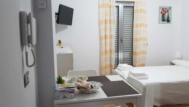 A hotel room with a bed, a desk with a chair, a telephone, a television, and a window with curtains.