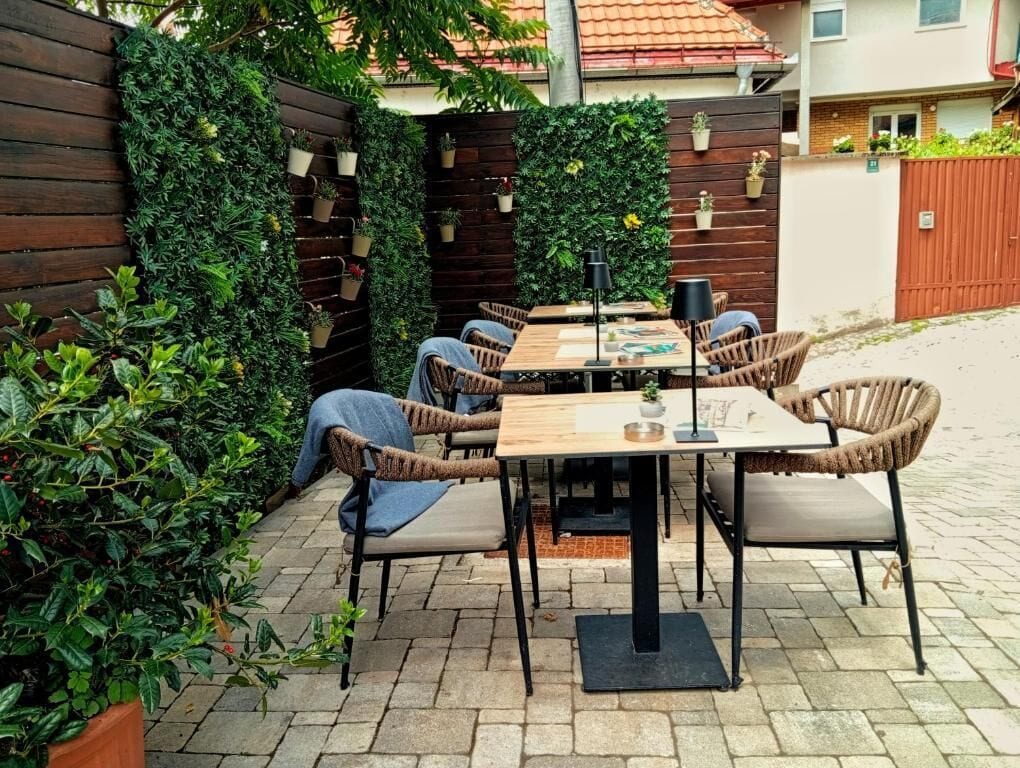 Un patio al aire libre con una mesa de madera y sillas de mimbre, rodeado de abundante vegetación y una valla de madera.