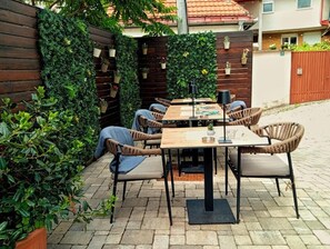 An outdoor patio with a wooden table and wicker chairs, surrounded by lush greenery and a wooden fence. - Hotel Boss (Sarajevo)