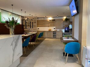 A modern interior with a marble reception desk, blue chairs, a kitchen area, and a flat-screen TV mounted on the wall. - Hotel Boss (Sarajevo)