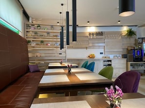 A modern dining area with a long table, cushioned seating, pendant lighting, and a kitchen area in the background. - Hotel Boss (Sarajevo)