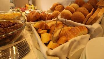 A buffet with various food items including bread rolls, a glass bowl of salad, and utensils.