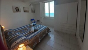 A bedroom with a bed, a chair, a wardrobe, and a window with a view.