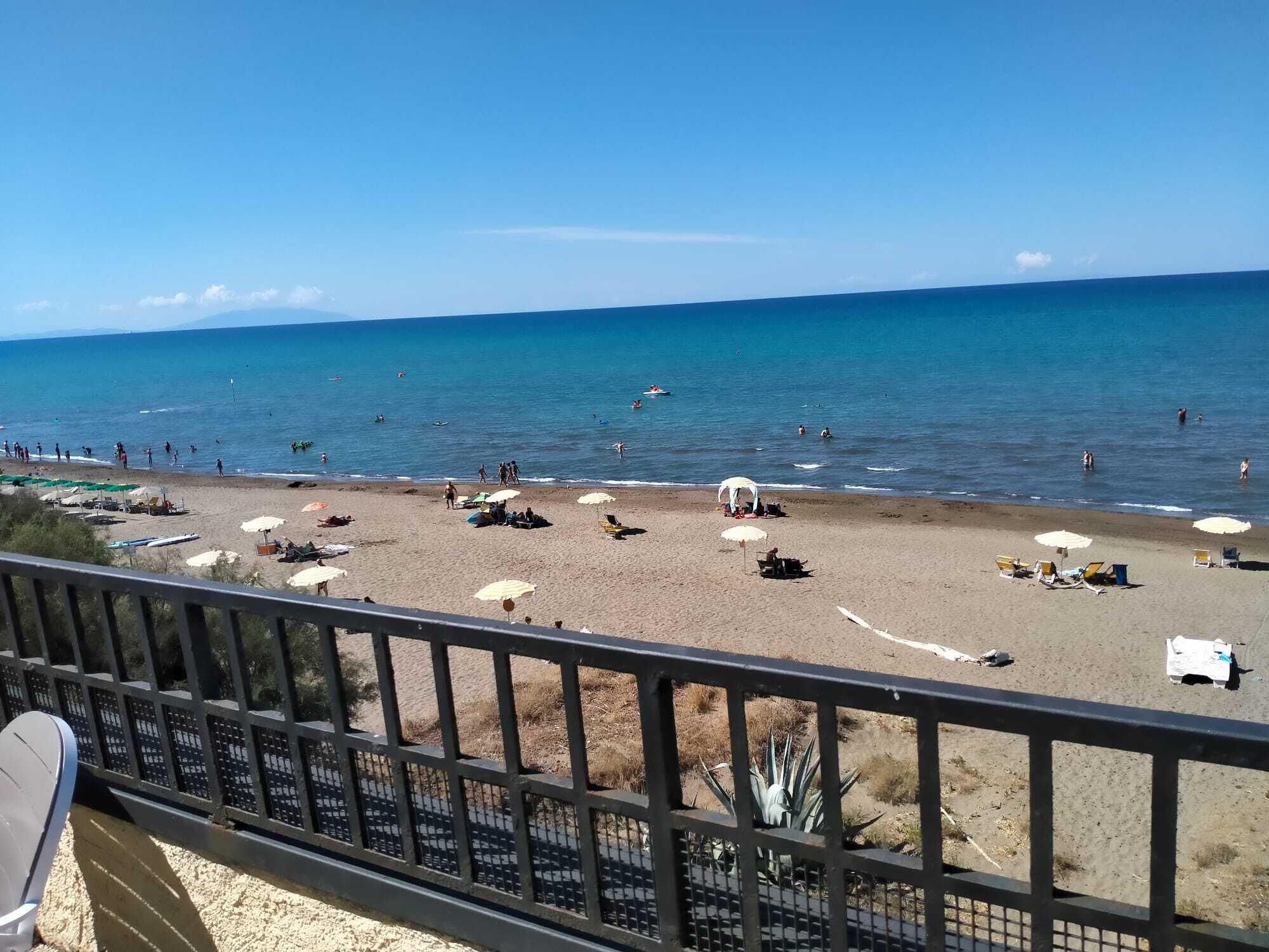 A beach with umbrellas and sun loungers, a railing, and a clear view of the ocean.