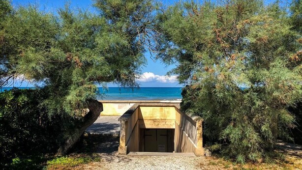 A beachside structure with a door, surrounded by trees and overlooking the sea.