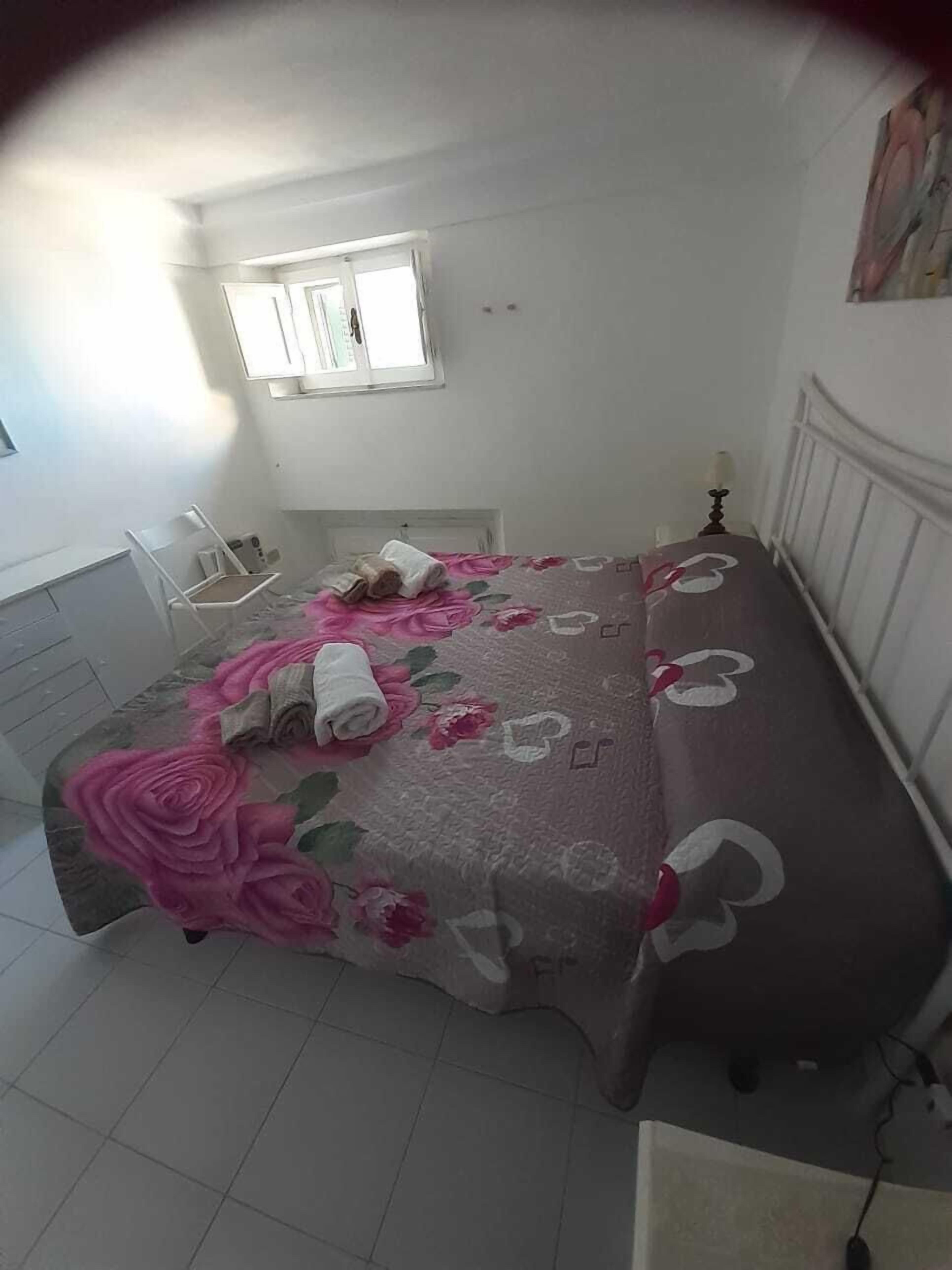 A bedroom with a bed, a chair, a window, and a painting on the wall.