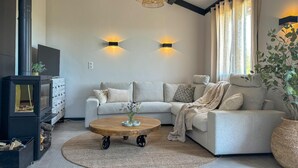 Ein modernes Wohnzimmer mit einem Ecksofa, einem Holztisch, einem Kamin und einem großen Fenster mit Vorhängen.