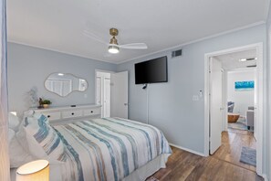 A bedroom with a bed, a ceiling fan, a TV, a mirror, and a door leading to another room. - Poolside Destin Condo + Free Beach Service (Destin)