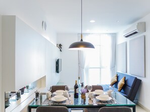A modern dining area with a glass table set for four, a sofa with cushions, and an air conditioning unit on the wall.
