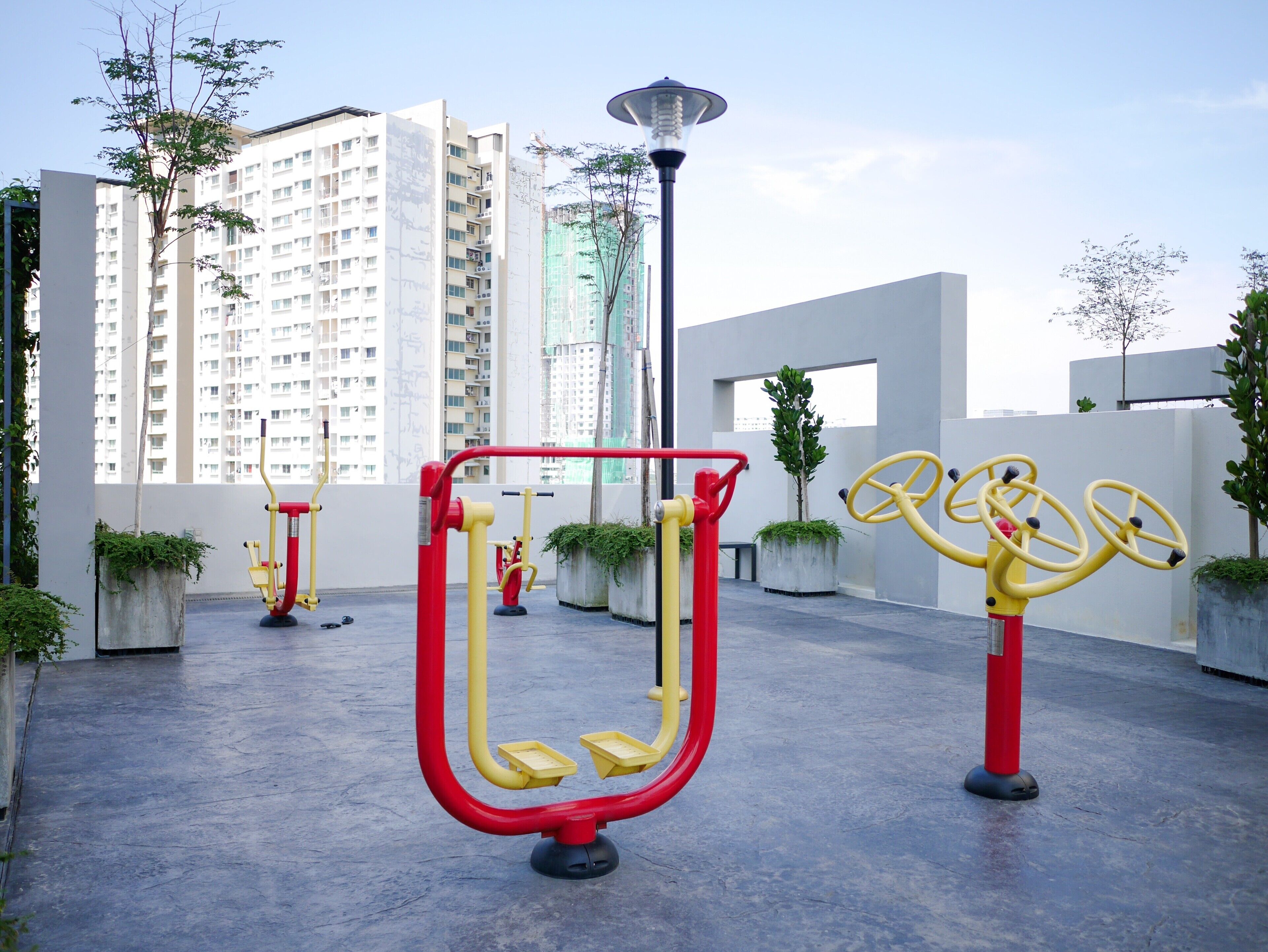 Des appareils de musculation en plein air, des plantes en pot et un lampadaire dans un environnement urbain.