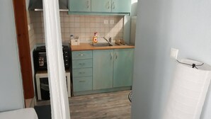 Een compacte keuken met blauwgroene kastjes, een gootsteen en een aanrecht.