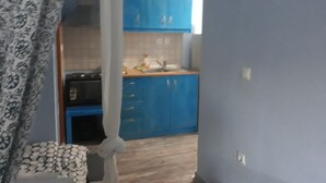 Een kamer met een gordijn met patroon, een bed en uitzicht op een keuken met blauwe kasten.