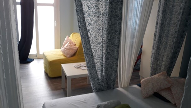 Een kamer met een bed, een klein tafeltje, een gele bank en gordijnen met een patroon.