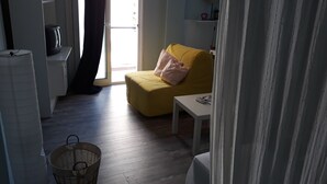 Een kamer met een gele bank, een witte tafeltje en een rieten mand.