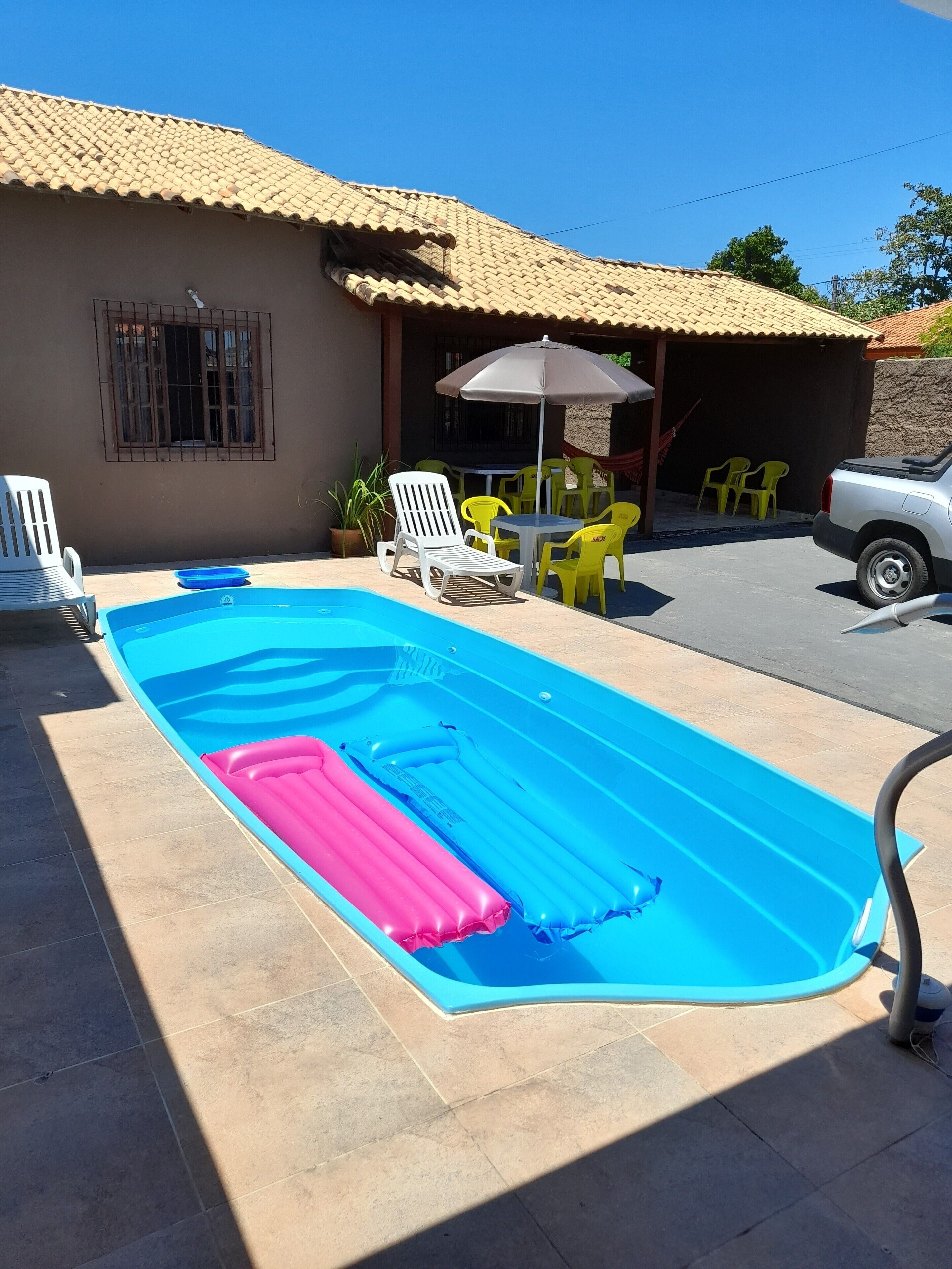 A swimming pool with inflatable loungers, a table with chairs, and a covered area with a table and chairs.