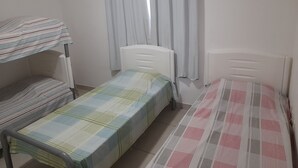 A dormitory room with bunk beds, a single bed, a radiator, and a window with curtains. - Itaipuaçu Residências Cajueiros II (Maricá)