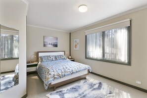 A bedroom with a bed, bedside tables, a nightstand, a window with curtains, and a ceiling light.