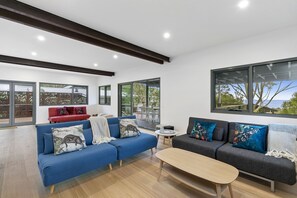 Ein modernes Wohnzimmer mit zwei Sofas, einem Couchtisch und großen Fenstern mit Blick ins Freie.