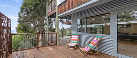 A wooden deck with two striped lounge chairs, a metal railing, and a view of a tree and building.