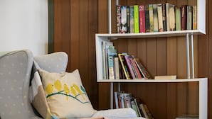 Een kamer met een grijze fauteuil, een boekenplank vol boeken en een wand van houten panelen.