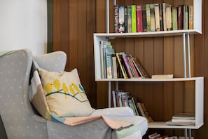 Una habitación con un sillón gris, una estantería llena de libros y un panel de pared de madera.