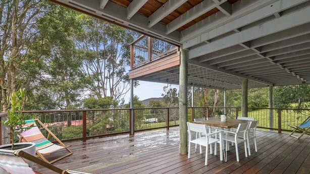 Een terras buiten met een tafel en stoelen, omgeven door een balustrade en bomen.