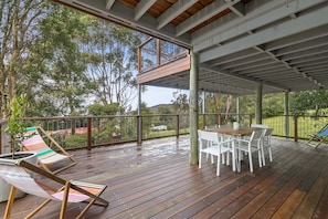 An outdoor deck with a table and chairs, surrounded by a railing and trees.