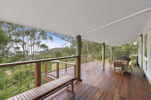A wooden deck with a bench and table, overlooking a forested area.