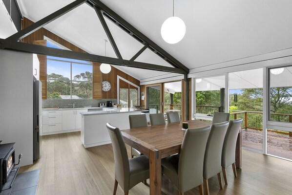 A modern kitchen with a central island, dining area with chairs, and large windows offering a view of the outdoors.