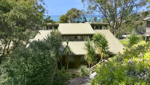 Een twee verdiepingen tellend huis met een plat dak, omringd door weelderige begroeiing en uitzicht op zee.