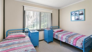 Een slaapkamer met twee eenpersoonsbedden, een raam met gordijnen, een bureau met stoel, en een aan de muur hangend schilderij.