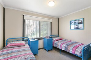 Un dormitorio con dos camas individuales, una ventana con cortinas, un escritorio con una silla y un cuadro colgado en la pared.