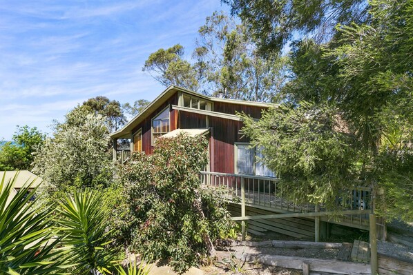 A two-story house with a balcony, surrounded by dense vegetation.